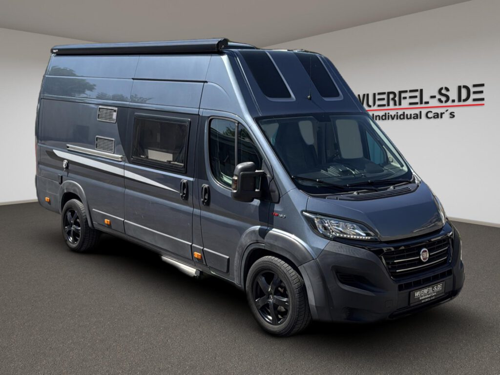 Grauer Campingkastenwagen mit zwei Dachfenstern über dem Fahrerhaus und seitlicher Markise, von schräg vorn.