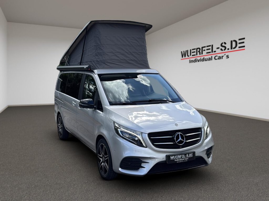 Silberner Mercedes Campingbus mit geöffnetem Aufstelldach und seitlicher Markise, in Dreiviertelansicht von vorn.